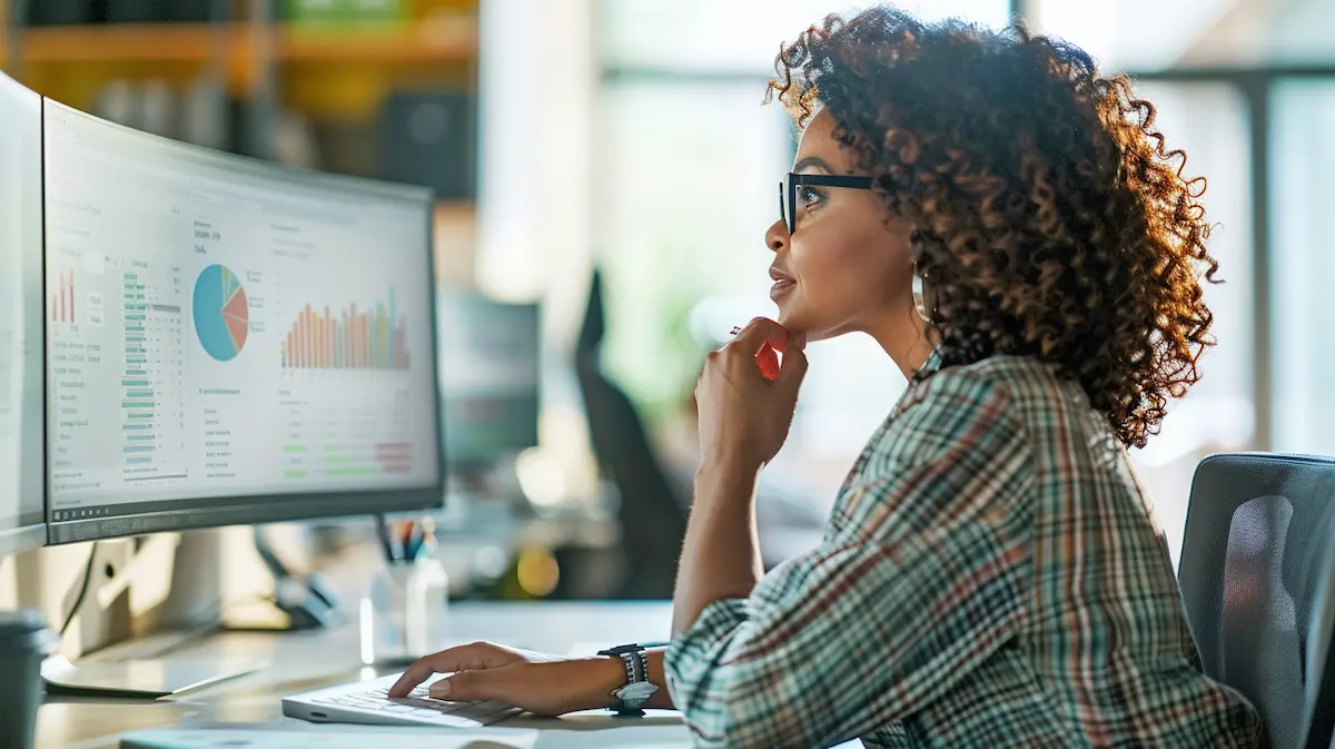 Small business owner reviewing colorful financial dashboards and KPI charts on a monitor — illustrating a small business benchmarking guide for comparing numbers to industry peers