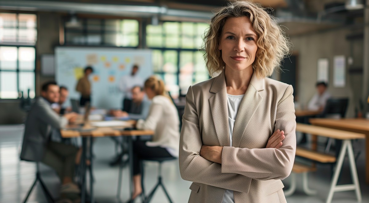 Thumbnail: Business leader standing confidently with arms crossed while team collaborates in background - handling toxic employees in small business culture
