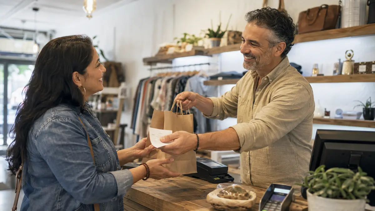 Small business store owner handing a purchase to a customer at the counter
